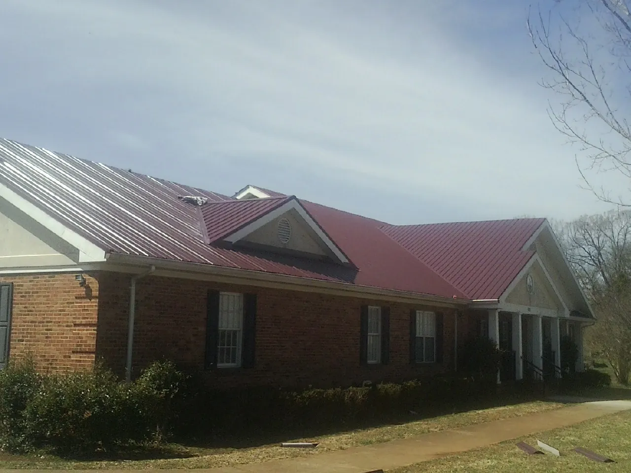 Red metal roof with gabled entries on a long brick building, from a Hail Damage Roof Repair job in Willis