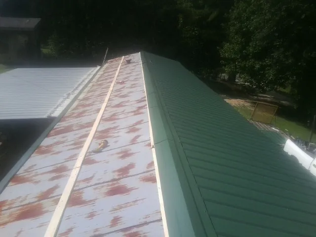 Old rusted panels beside newly installed green metal roofing — Wind Damage Roof Repair by Roofing Brothers in Willis